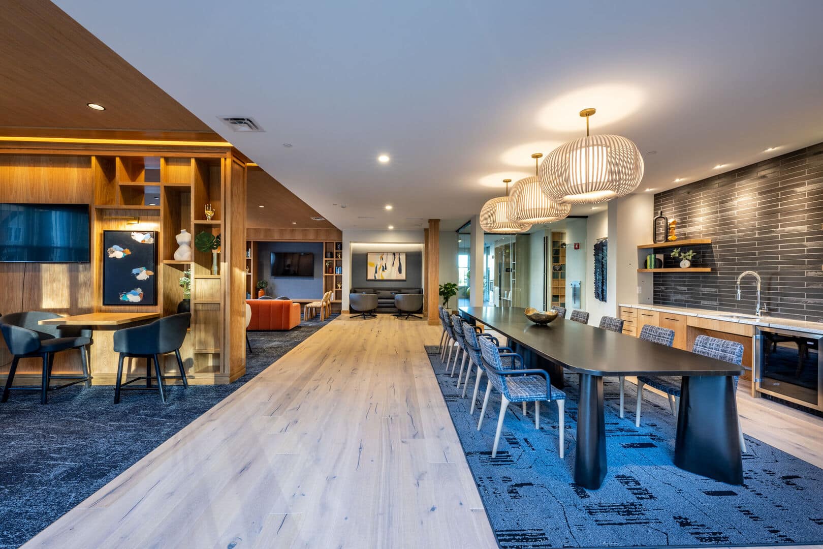 Modern community space featuring long dining table, pendant lights, and open-concept lounge layout