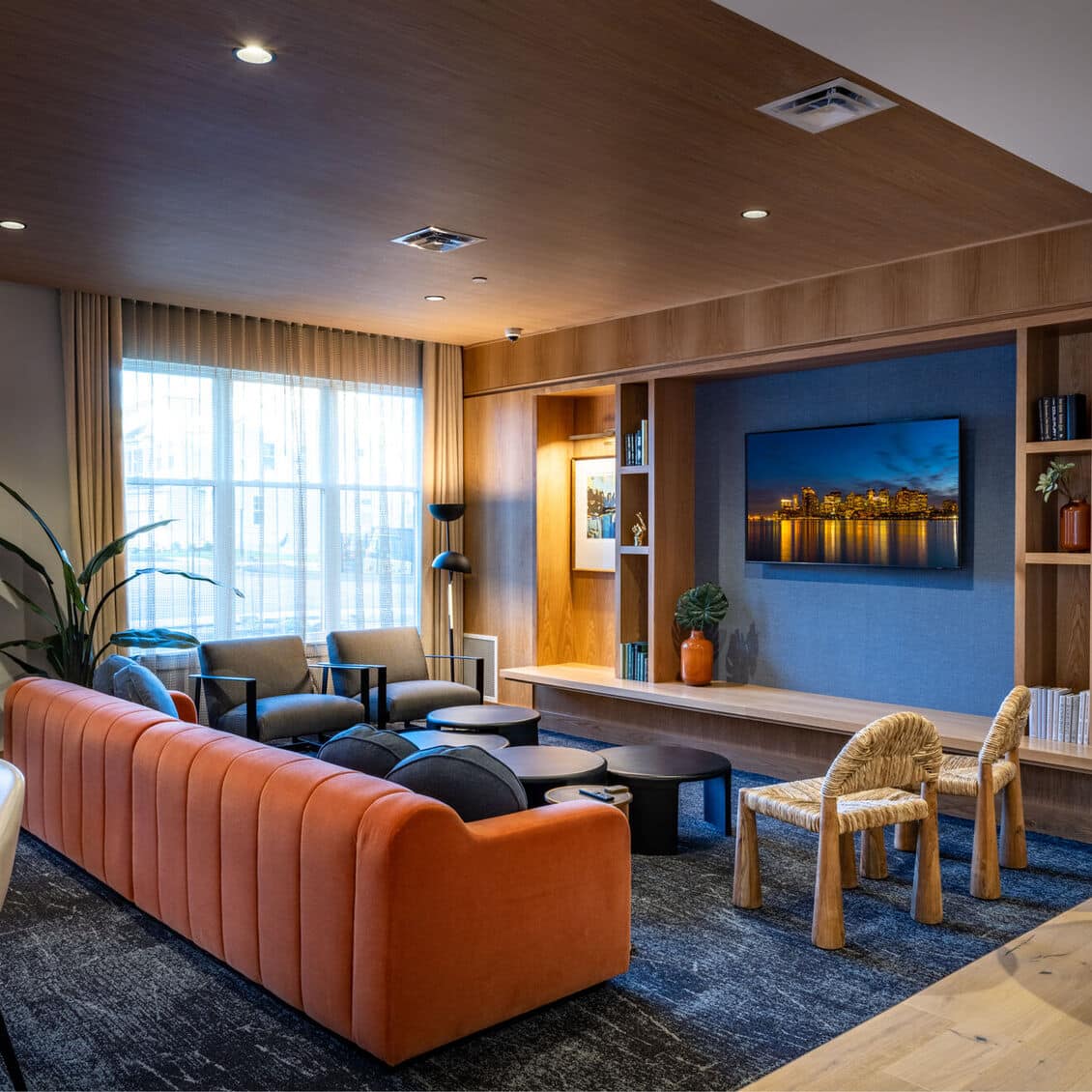 Cozy resident lounge with orange sofa, modern chairs, and wall-mounted television in wood paneling
