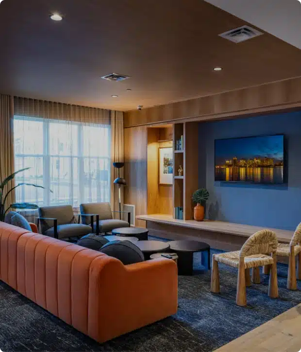 Stylish apartment lounge at The Apartments at Cold Brook Crossing in Sudbury, MA. orange couch, cozy seating, and wall-mounted cityscape artwork