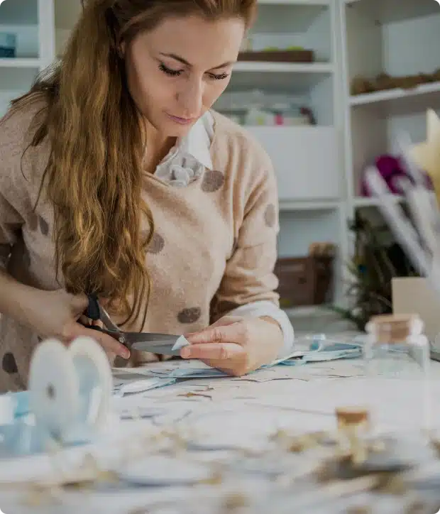 Woman focused on crafting project at ribbon-covered table with scissors and materials