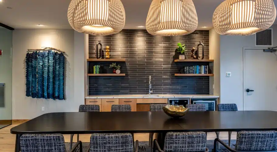 Elegant dining lounge with black table, kitchenette, and modern pendant light fixtures overhead
