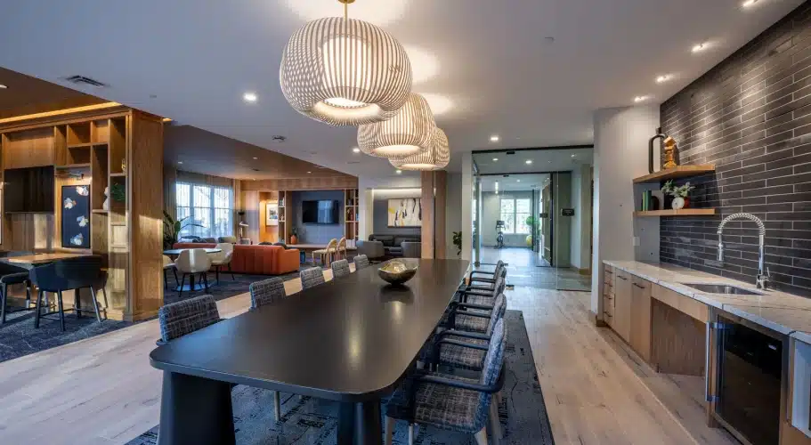 The Apartments at Cold Brook Crossing in Sudbury, MA, sleek lounge room with kitchenette, black tile backsplash, and modern decorative lighting.