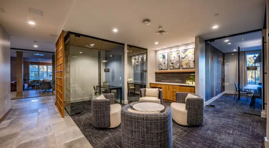 The Apartments at Cold Brook Crossing in Sudbury, MA, work from home hub featuring a business lounge with private work rooms, modern lighting, and cozy circular guest seating.