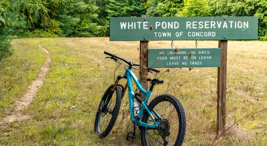 Bicycle resting at White Pond Reservation sign with wooded trail in Concord conservation land