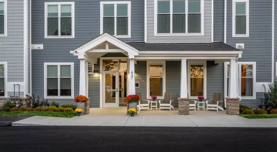 Front entry of apartment building with white columns, seasonal flowers, and inviting chairs