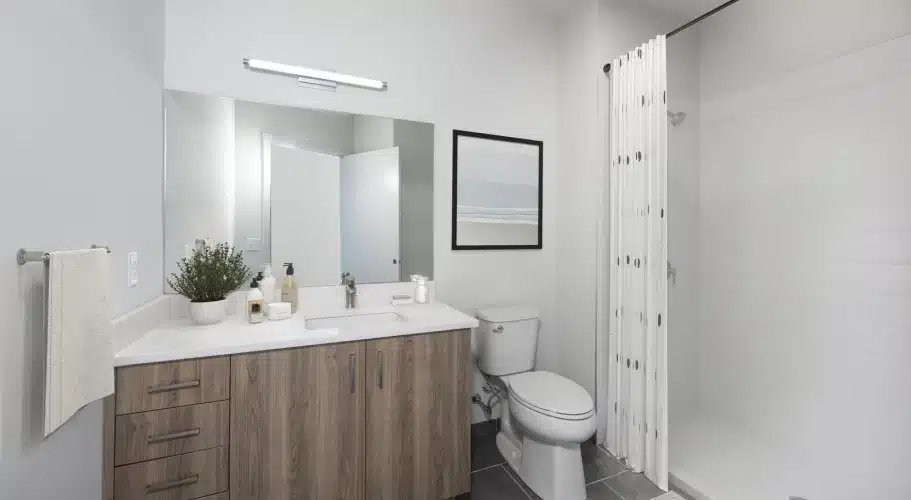 Bright bathroom with wood vanity, framed artwork, and white shower featuring polka-dot curtain