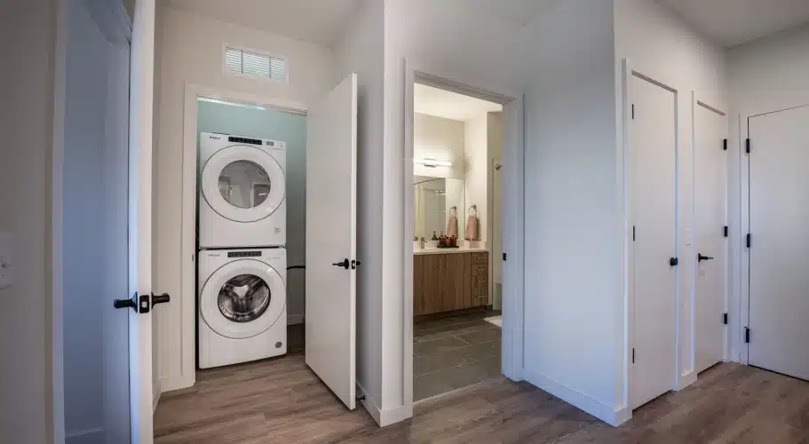 Apartment hallway featuring in-unit stacked washer dryer, access to bathroom, and multiple entryways