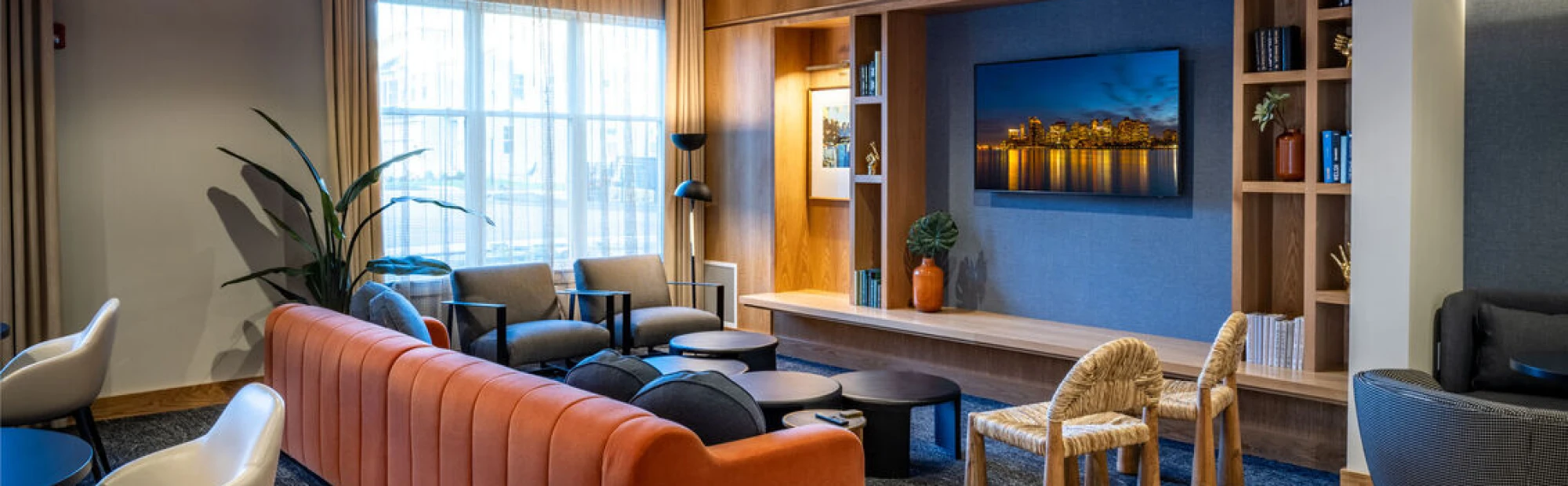 Elegant communal lounge with curved orange couch, multiple armchairs, and entertainment setup