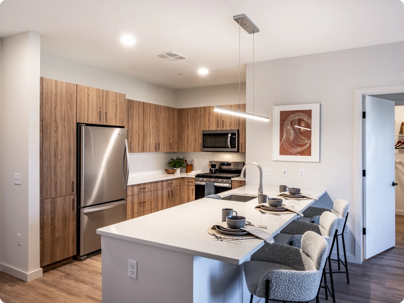 Contemporary apartment kitchen with wood cabinetry, stainless steel appliances, and breakfast bar seating