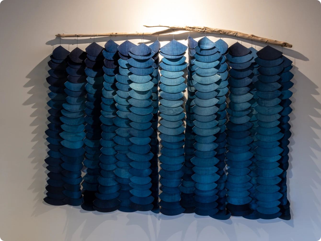 Artistic wall installation featuring layered blue fabric pieces suspended from a natural wood branch