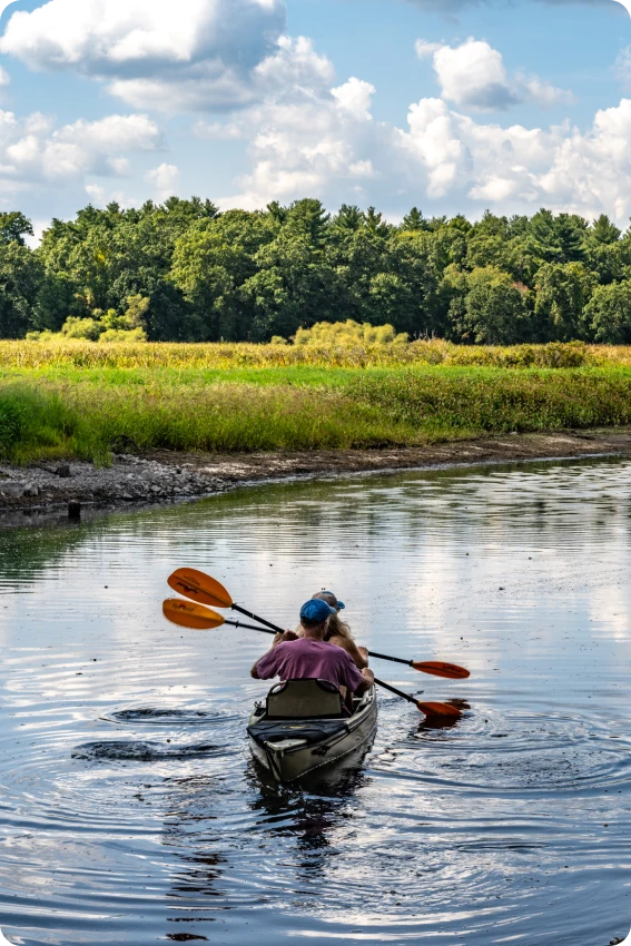 Rear view of couple kayaking through scenic waterway with paddles and rippling reflections