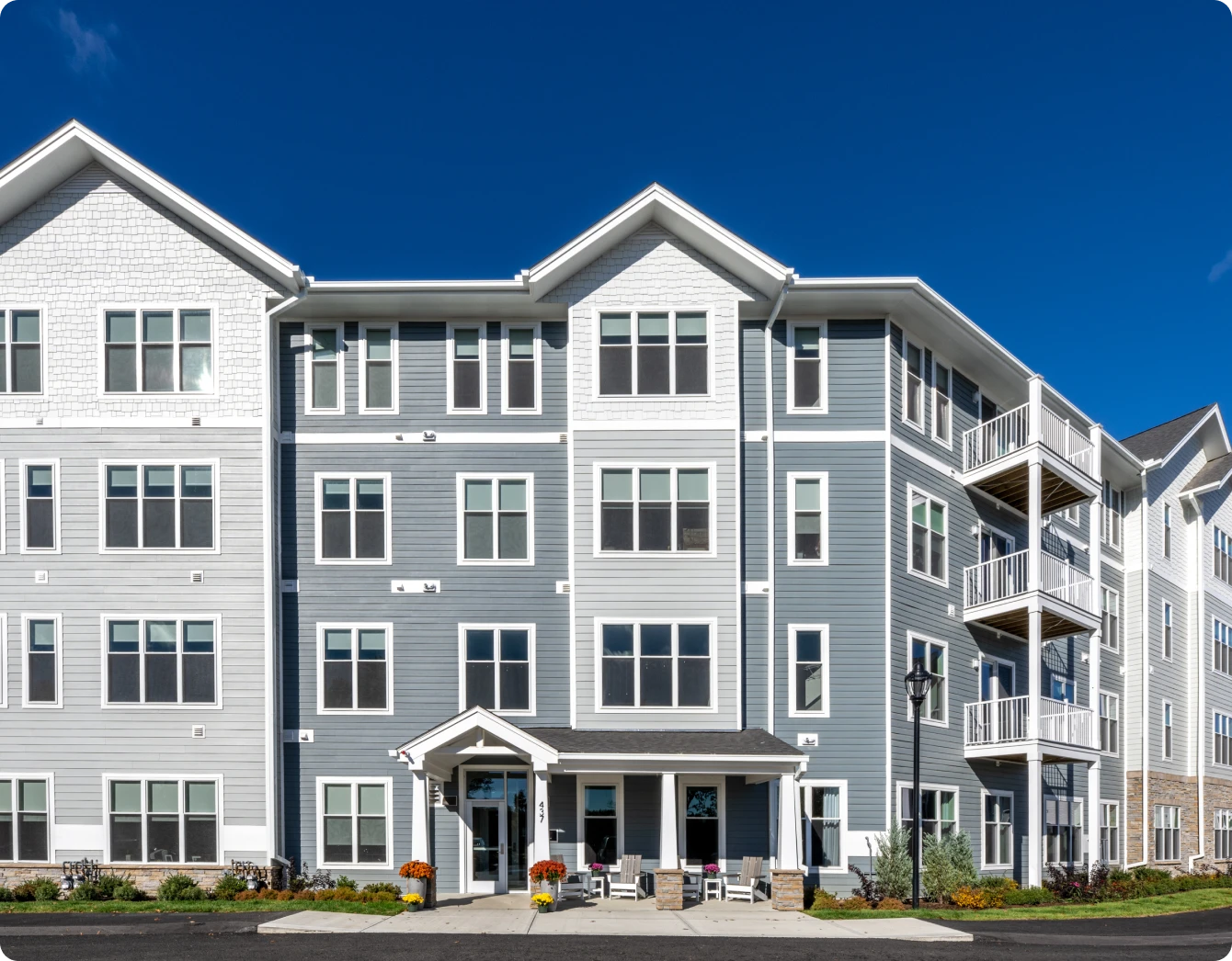 Multi-story gray apartment building with balconies, large windows, and a landscaped entrance