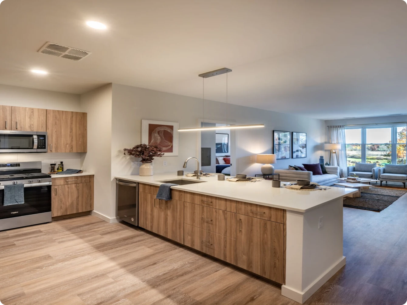 Open-concept apartment kitchen with wood cabinetry, island seating, and view into living room