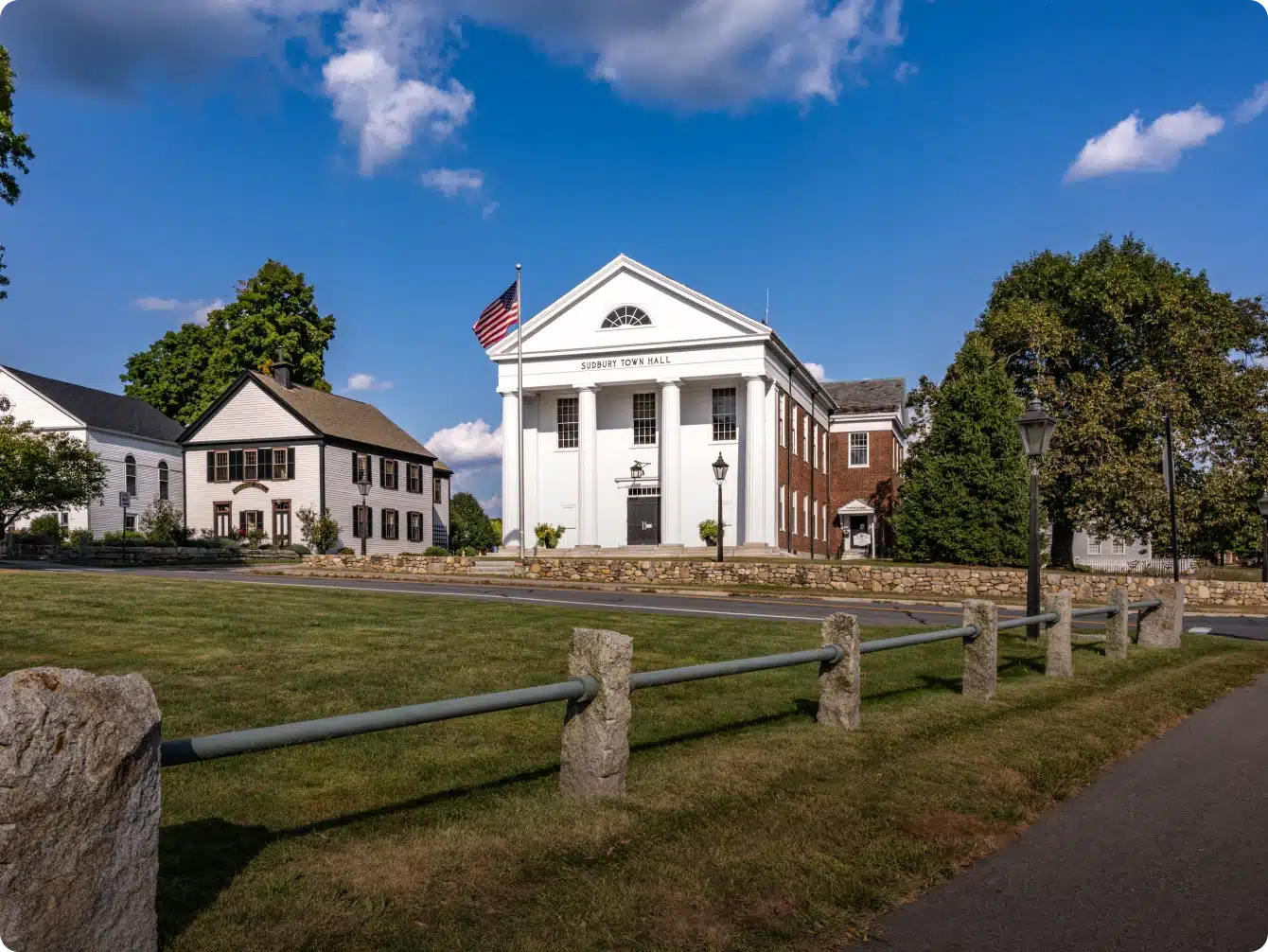 Sudbury Town Hall with American flag, white columns, and brick accents in civic green