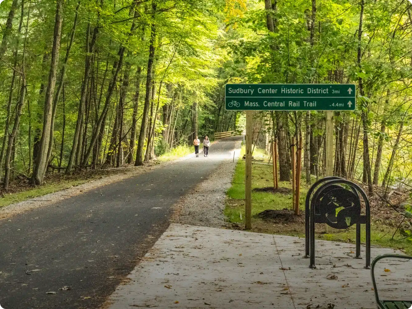 Forest path with two people walking past Sudbury Historic District trail sign