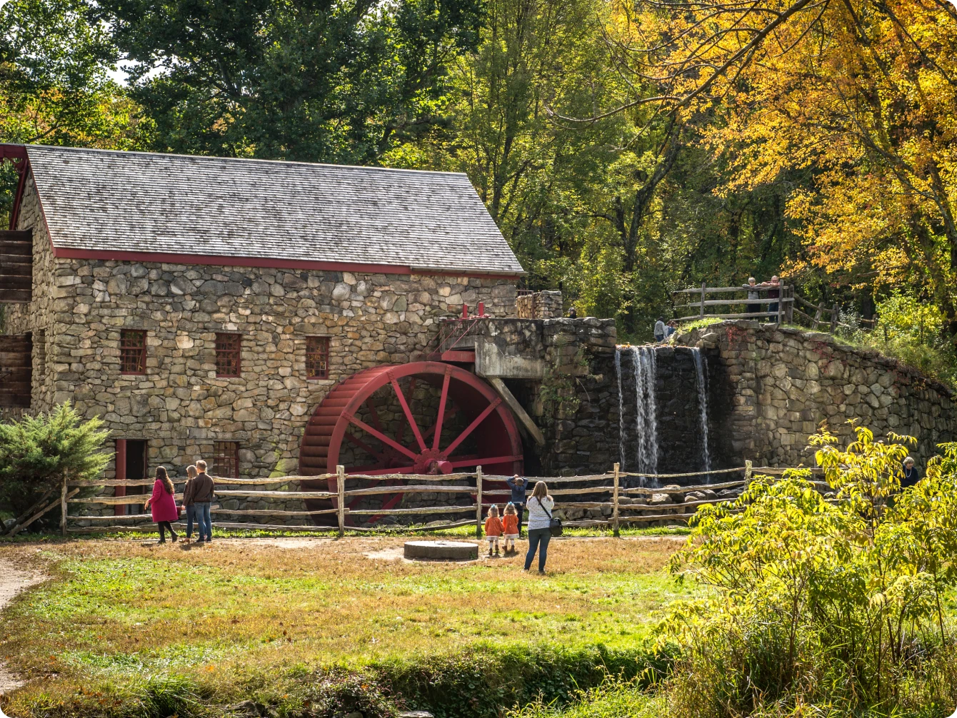 Scenic stone grist mill with red water wheel and waterfall surrounded by fall foliage