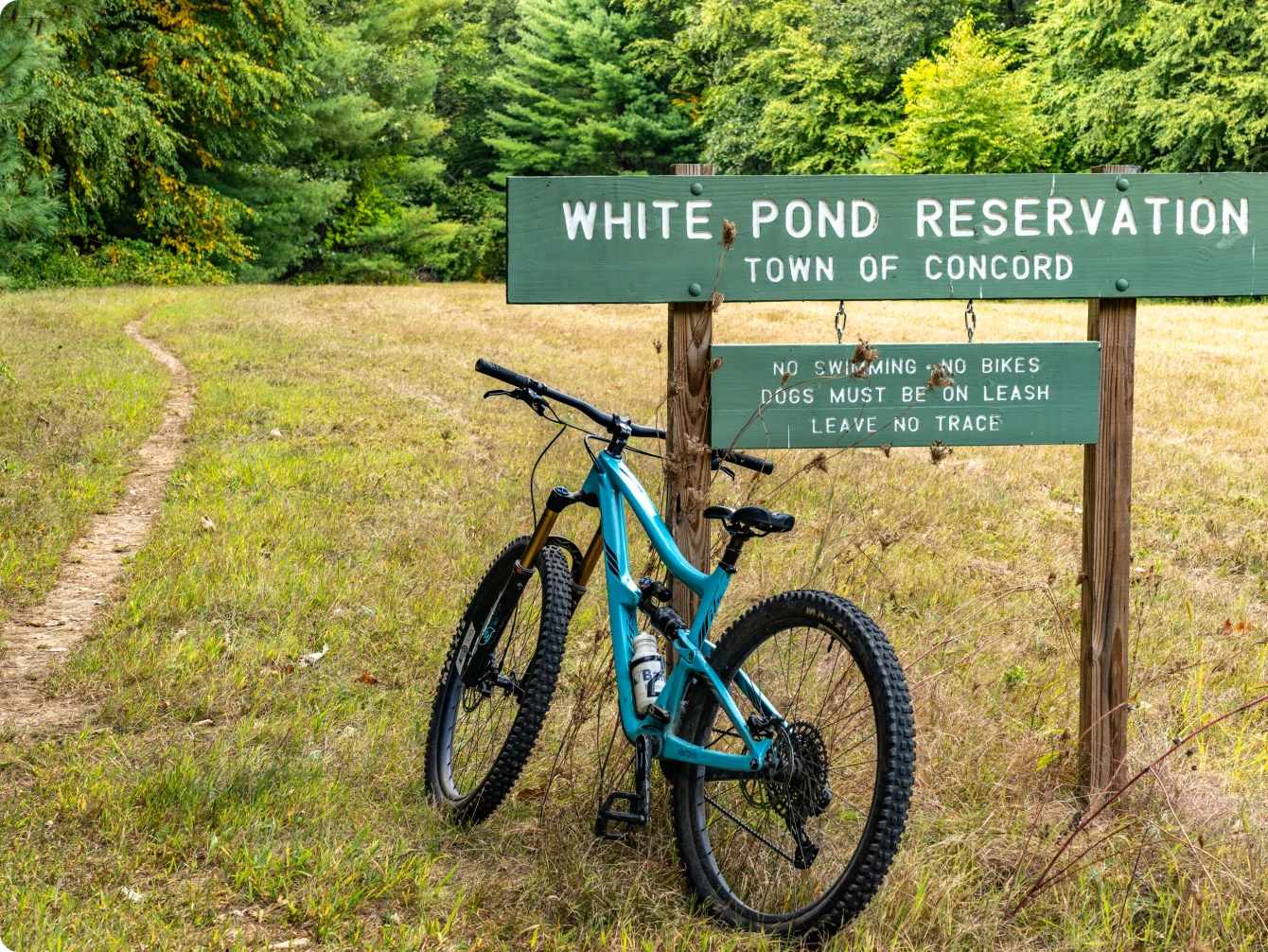 Green sign for White Pond Reservation in Concord with mountain bike parked beside it