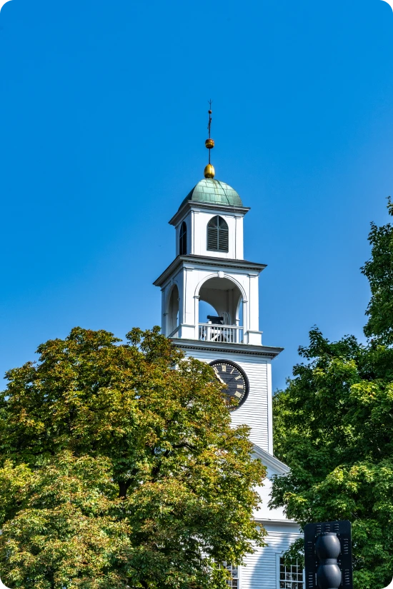 Classic white church with clock tower and green dome rising above leafy trees