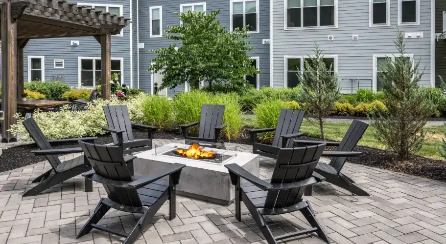 Outdoor fire pit surrounded by Adirondack lounge chairs on the patio at The Apartments at Cold Brook Crossing in Sudbury, MA.