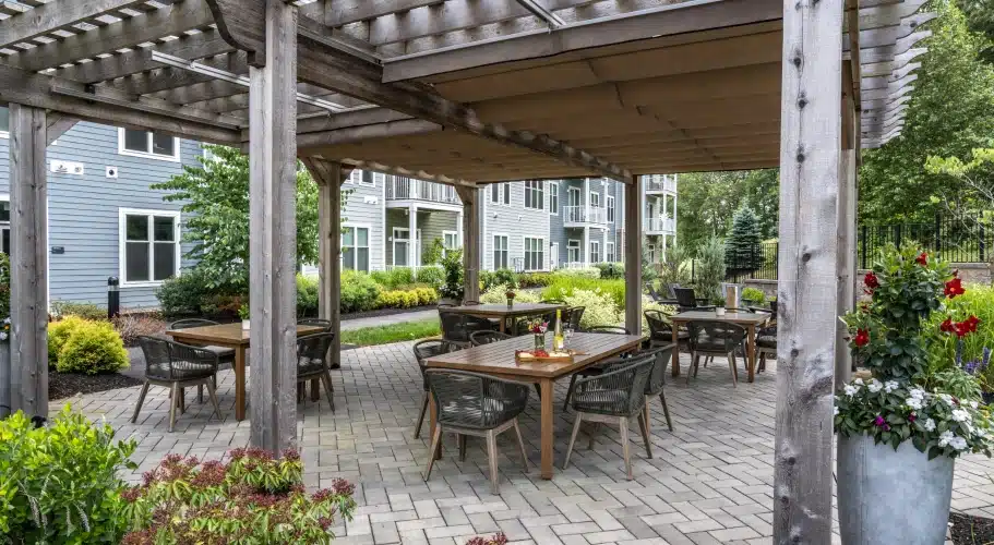 Three-season patio with pergola, dining tables, and garden views at The Apartments at Cold Brook Crossing in Sudbury, MA.