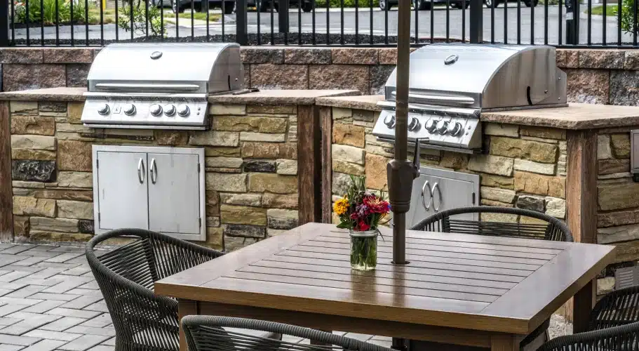 Two built-in stainless steel grills with stone base and outdoor dining table at The Apartments at Cold Brook Crossing in Sudbury, MA.