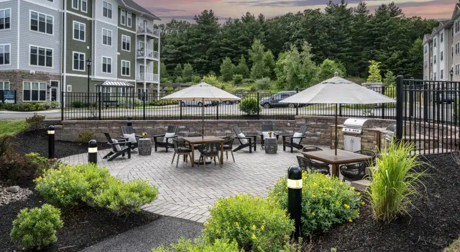 Outdoor grilling and lounge area with patio seating and umbrellas at The Apartments at Cold Brook Crossing in Sudbury, MA