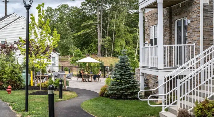 Outdoor grilling and lounge area with patio seating and umbrellas at The Apartments at Cold Brook Crossing in Sudbury, MA