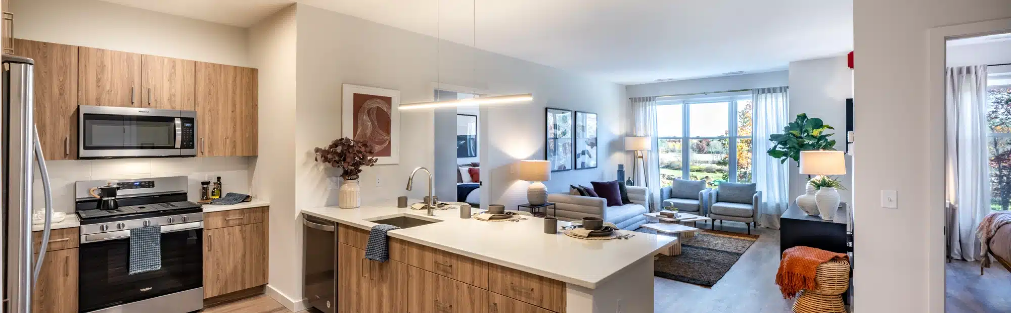 Cozy apartment living room featuring modern art, plush seating, and view of trees through window at The Apartments at Cold Brook Crossing